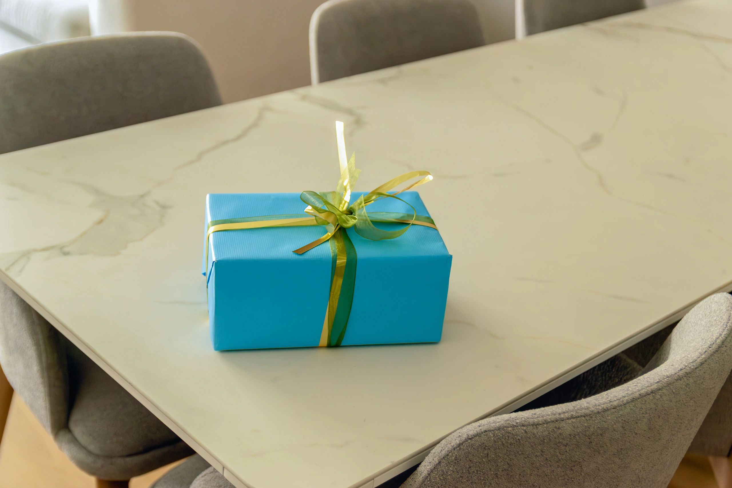 High angle view of a blue gift box with a gold ribbon on a marble dining table.